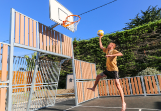 Mand spiller basketball på ferieparken Flower Camping Le Vieux Moulin i Bretagne, Frankrig, under blå himmel.
