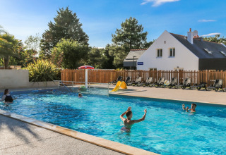 Udendørs swimmingpool med familier der svømmer, solrige omgivelser i Flower Camping Le Vieux Moulin, Bretagne.