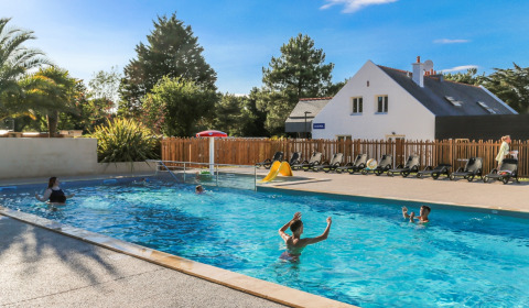 Udendørs swimmingpool med familier der svømmer, solrige omgivelser i Flower Camping Le Vieux Moulin, Bretagne.