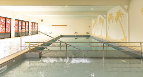 Indoor swimming pool with palm tree wall art and red windows at Flower Camping Le Vieux Moulin in Brittany, France.