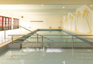 Indoor swimming pool with palm tree wall art and red windows at Flower Camping Le Vieux Moulin in Brittany, France.