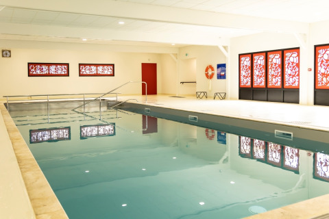 Indendørs swimmingpool med røde vinduesdekorationer på Flower Camping Le Vieux Moulin i Bretagne, Frankrig.