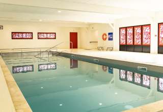 Hallenbad mit roten Fensterdekorationen im Flower Camping Le Vieux Moulin in der Bretagne, Frankreich.