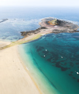Luchtfoto van strand en zeewater bij Erquy, Bretagne, Frankrijk, met kleine boten op het heldere turquoise water.