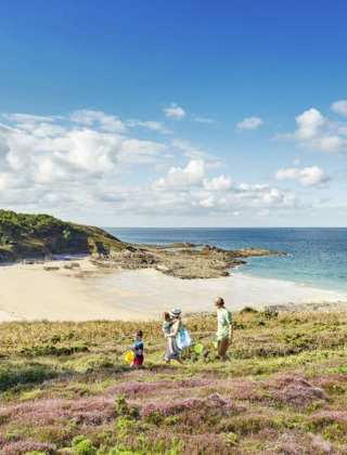 Gezin loopt langs een schilderachtig kustpad bij een strand in Erquy, Bretagne, onder een blauwe lucht.