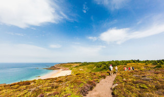 Wandelaars op een kustpad nabij Erquy in Bretagne, Frankrijk, met uitzicht op zee en duinlandschap.