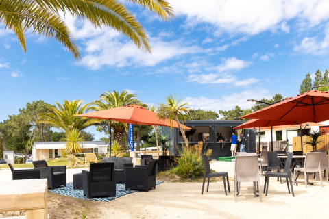 Udendørs loungeområde med palmer, parasoller og moderne siddepladser på Flower Camping Le Vieux Moulin i Bretagne.