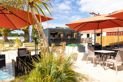 Outdoor lounge area with umbrellas, tables, and greenery at Flower Camping Le Vieux Moulin in Brittany, France.
