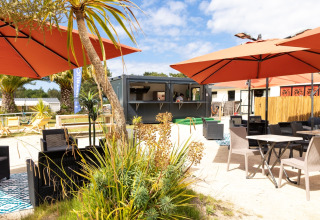 Outdoor lounge area with umbrellas, tables, and greenery at Flower Camping Le Vieux Moulin in Brittany, France.