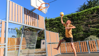 Jonge man speelt basketbal op het buitenveld van Flower Camping Le Vieux Moulin in Bretagne, Frankrijk.