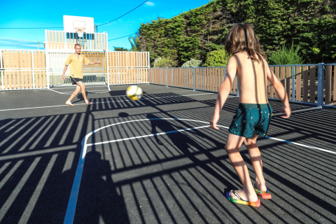 Vater und Sohn spielen Ball auf einem Outdoor-Sportplatz im Flower Camping Le Vieux Moulin in der Bretagne.