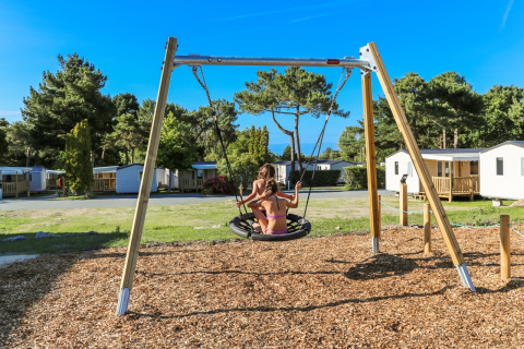 Bambini giocano su un’altalena nel parco giochi di Flower Camping Le Vieux Moulin in Bretagna, Francia.