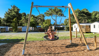 Kinderen spelen op een schommel bij de speeltuin van Flower Camping Le Vieux Moulin in Bretagne, Frankrijk.