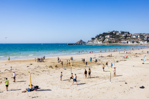 Playa en Flower Camping Le Vieux Moulin en Bretaña, Francia, con gente jugando voleibol y disfrutando del mar.