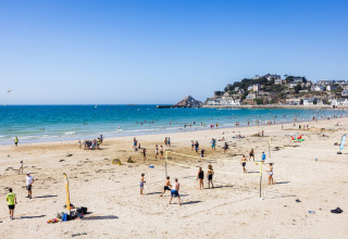 Plage du Flower Camping Le Vieux Moulin en Bretagne, France, avec des gens jouant au volley-ball et se baignant.