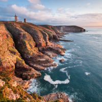 Imposante kliffen en vuurtoren aan de kust bij Erquy in Bretagne, Frankrijk, onder zacht zonlicht.