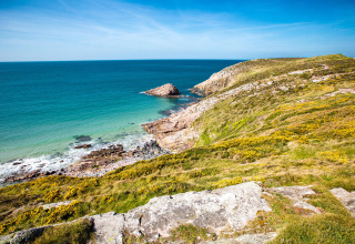 Kystudsigt ved Flower Camping Le Vieux Moulin i Bretagne, Frankrig, med blå hav og grøn bakke.