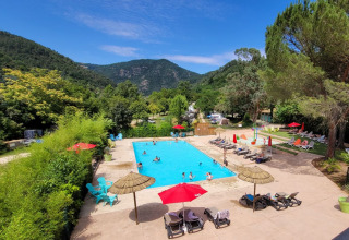 Buitenzwembad bij Flower Camping Mas de Champel, omringd door bergen in Auvergne-Rhône-Alpes, Frankrijk.