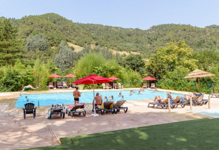 Außenpool im Flower Camping Mas de Champel mit Gästen, Sonnenliegen und Bergen in Auvergne-Rhône-Alpes.