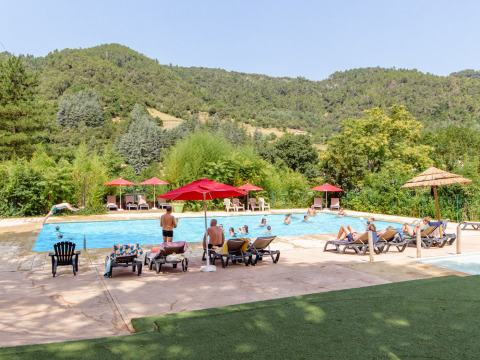 Außenpool im Flower Camping Mas de Champel mit Gästen, Sonnenliegen und Bergen in Auvergne-Rhône-Alpes.