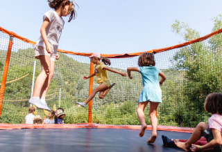 Kinder springen fröhlich auf einem Trampolin im Flower Camping Mas de Champel, Auvergne-Rhône-Alpes, Frankreich.