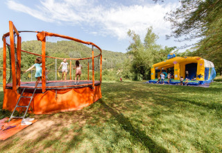 Children play on a trampoline and bouncy castle at Flower Camping Mas de Champel holiday park in France.