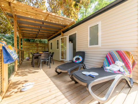 Wooden deck with sun loungers and dining table at Flower Camping Mas de Champel in Auvergne-Rhône-Alpes, France.