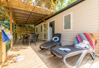 Wooden deck with sun loungers and dining table at Flower Camping Mas de Champel in Auvergne-Rhône-Alpes, France.