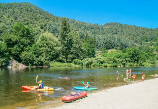 Bambini giocano e remano in kayak in un fiume circondato da colline verdi al Flower Camping Mas de Champel, Francia.