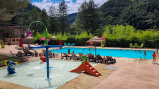 Piscine extérieure avec espace enfants et transats au Flower Camping Mas de Champel en Auvergne-Rhône-Alpes.