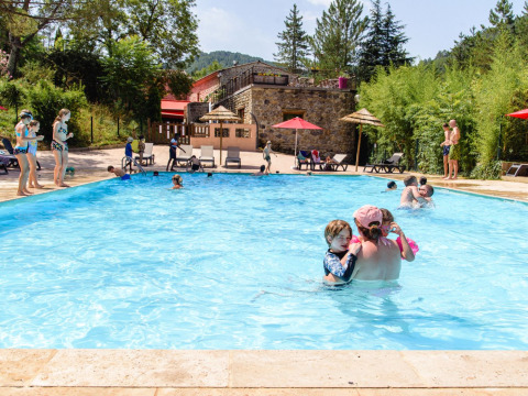 Familier og børn leger i en udendørs swimmingpool på Flower Camping Mas de Champel i Auvergne-Rhône-Alpes.