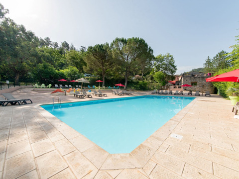 Außenpool mit Sonnenliegen und roten Sonnenschirmen im Flower Camping Mas de Champel, Auvergne-Rhône-Alpes, Frankreich.
