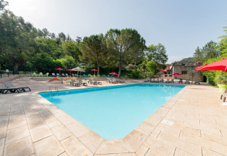 Piscina all'aperto con lettini e ombrelloni rossi al Flower Camping Mas de Champel, Alvernia-Rodano-Alpi, Francia.