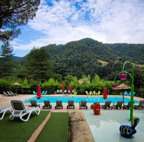 Piscine extérieure avec transats, aire de jeux et vue sur les montagnes au camping en Auvergne-Rhône-Alpes, France.