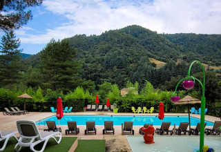 Piscine extérieure avec transats, aire de jeux et vue sur les montagnes au camping en Auvergne-Rhône-Alpes, France.