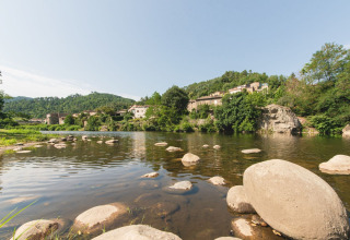 Río con rocas y casas rodeadas de vegetación, en Flower Camping Mas de Champel, Auvernia-Ródano-Alpes, Francia.