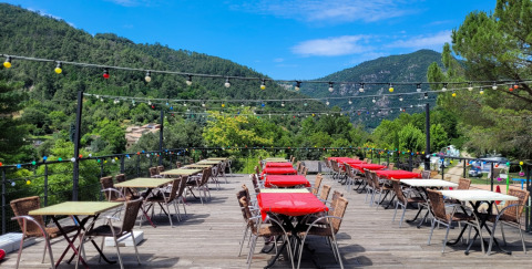 Terrasse mit bunten Tischen bei Flower Camping Mas de Champel, umgeben von grünen Bergen in Frankreich.