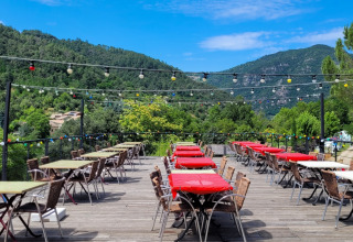 Udendørs restaurantterrasse ved Flower Camping Mas de Champel med farverige duge og udsigt til bjerge.