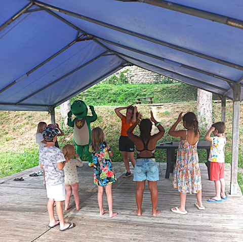 Kinderen doen mee aan een activiteit onder een tent met een dinosaurusmascotte bij Flower Camping Mas de Champel.