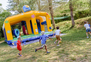 Kinderen spelen bij een grote springkussen op Flower Camping Mas de Champel in Frankrijk, omgeven door natuur.