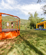 Children play on a trampoline and in a bounce house at Flower Camping Mas de Champel holiday park in France.