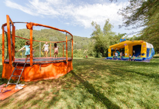 Children play on a trampoline and in a bounce house at Flower Camping Mas de Champel holiday park in France.