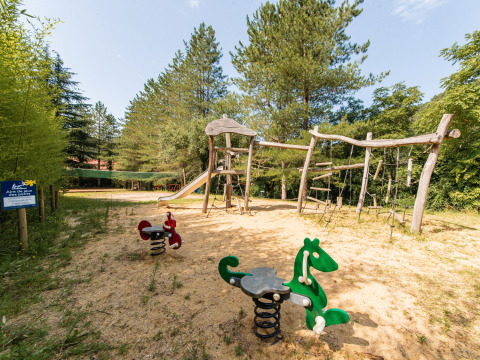 Spielplatz mit Holzgeräten und Wipptieren bei Flower Camping Mas de Champel in Auvergne-Rhône-Alpes, Frankreich.