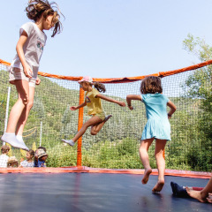 Children playing and jumping on a trampoline with safety net at a holiday park surrounded by French hills.