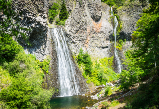 Beeindruckender Wasserfall mit üppigem Grün und Felsen in der Nähe von Les Ollières sur Eyrieux, Frankreich.