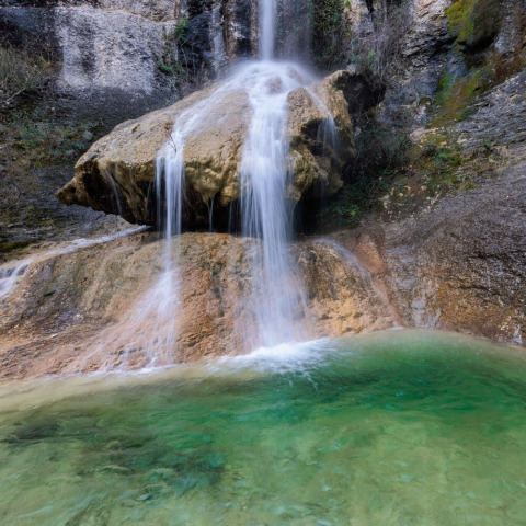 Cascada pintoresca que fluye sobre rocas junto a una piscina clara en Flower Camping Mas de Champel, Auvernia.