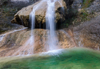 Cascata pittoresca che scorre sopra le rocce in una piscina verde a Flower Camping Mas de Champel, Auvergne-Rhône-Alpes.