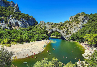 Arco natural de piedra sobre un río con bañistas y kayaks en Les Ollières sur Eyrieux, Auvernia-Ródano-Alpes.
