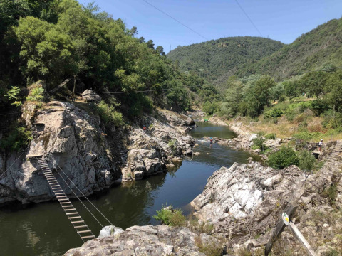 Vista de puentes de madera sobre el río en Flower Camping Mas de Champel, rodeado de colinas en Auvergne-Rhône-Alpes.