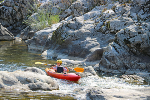 Bambino in kayak su un fiume roccioso al Flower Camping Mas de Champel, Auvergne-Rhône-Alpes, Francia.